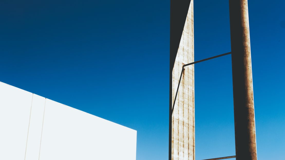 Structure métallique et mur blanc sur fond de ciel bleu, style architectural minimaliste.