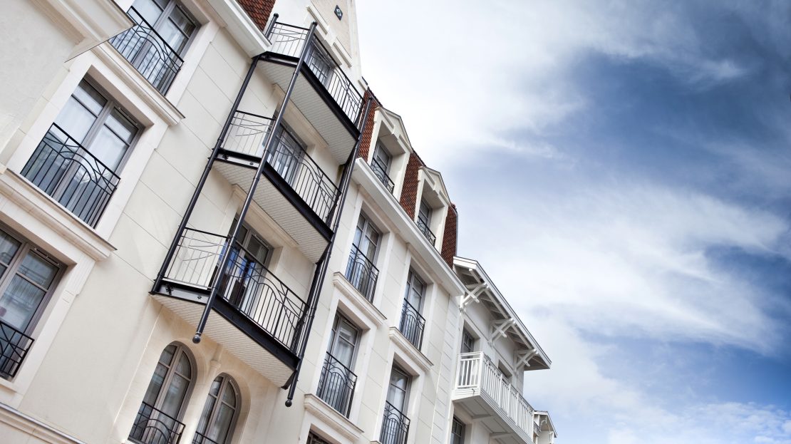 Façade d’une résidence de style haussmannien avec balcons en fer forgé sous un ciel nuageux.