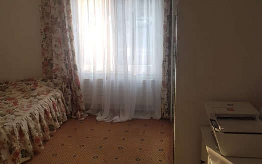 Chambre avec lit une place, moquette, rideaux à fleurs et lumière naturelle.