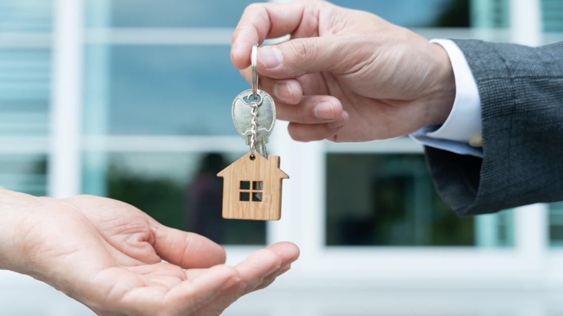 personne qui donne à une autre un porte clé avec une maison miniature