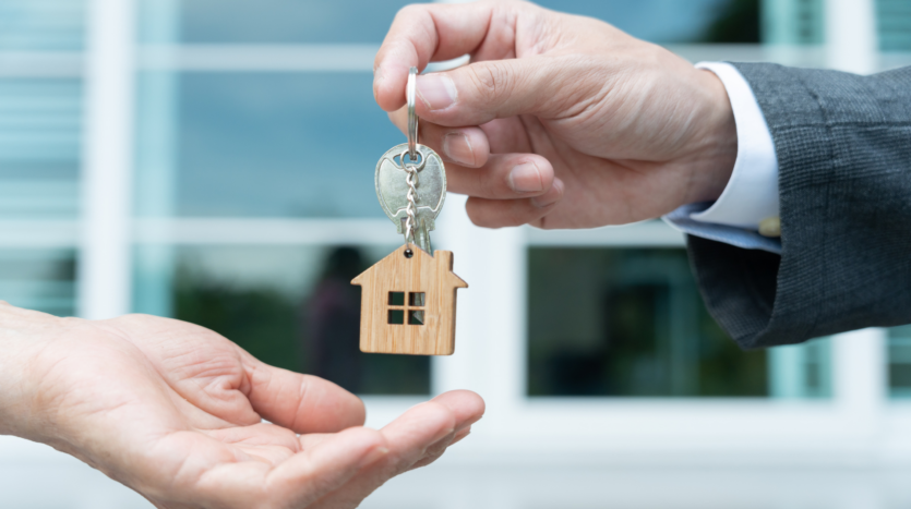 personne qui donne à une autre un porte clé avec une maison miniature